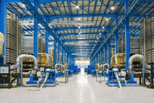 The vast and modern interior of the Taweelah RO Desalination Plant, showing rows of large-scale reverse osmosis units and piping under a blue steel structure.