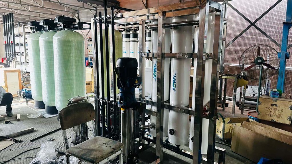 A robust industrial water treatment system being assembled in Globaluf's manufacturing facility, featuring multiple green FRP pre-treatment filter tanks, a high-pressure CNP pump, and white AOMAX membrane housings for RO or UF modules, all within a stainless steel frame.
